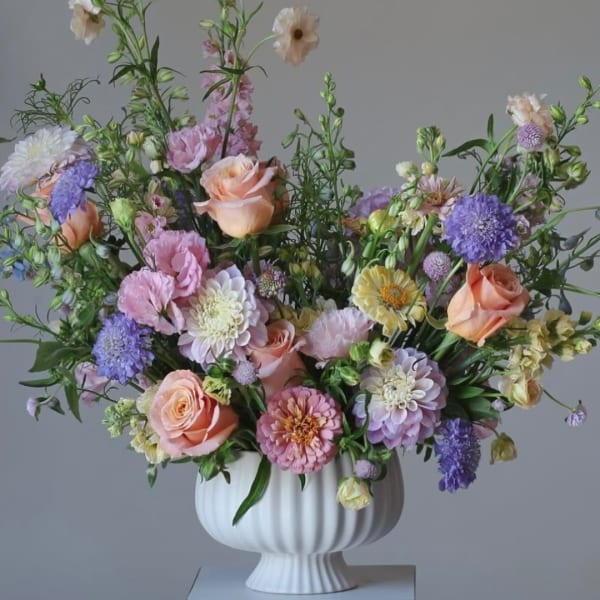Pastel mixed flower arrangement in a white pedestal vase