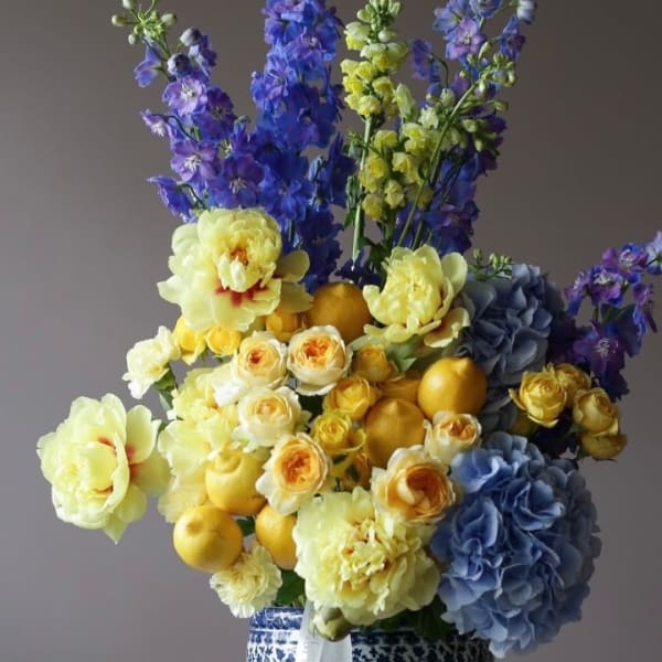 Bouquet of yellow and blue flowers with lemons in a patterned vase