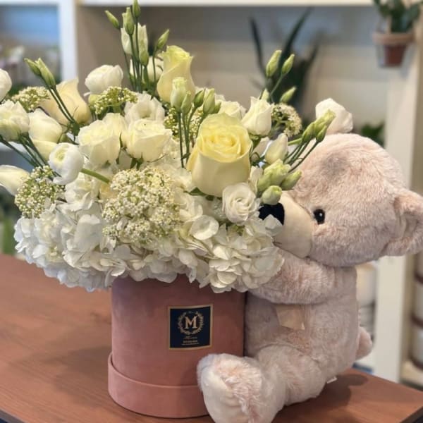 White floral arrangement in a pink hatbox with a teddy bear