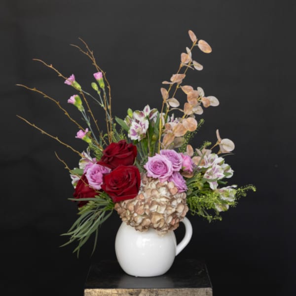 Mixed bouquet of red and pink roses in a white pitcher vase