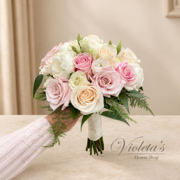 Pink and white rose bridal bouquet with greenery, held by a hand