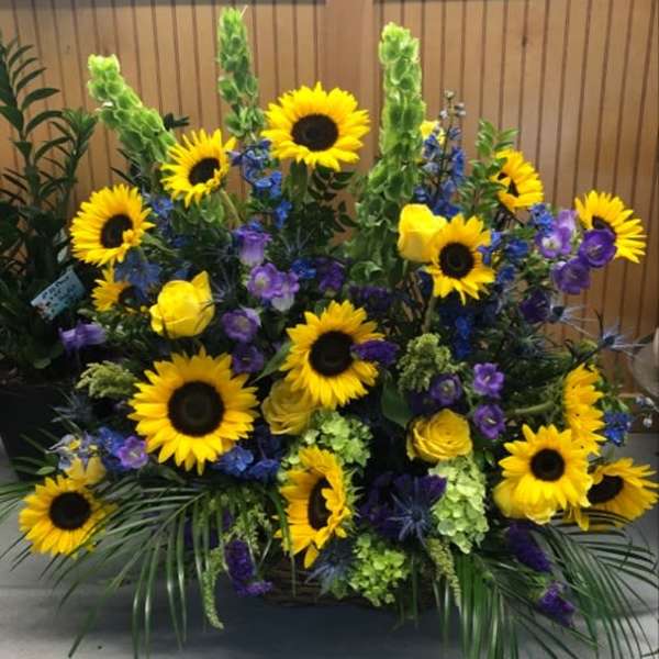 Large floral arrangement with sunflowers, yellow roses, and purple flowers