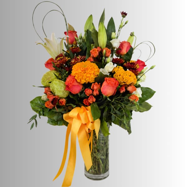 Mixed bouquet of roses, lilies, and marigolds in a glass vase with a yellow ribbon