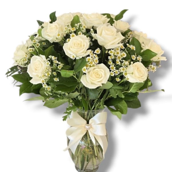 White roses and small daisies in a glass vase with a cream ribbon