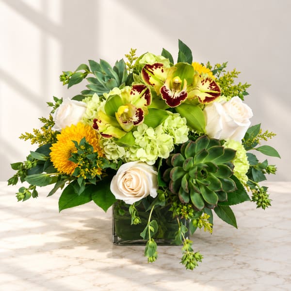 Mixed floral arrangement in a square glass vase with roses, orchids, and succulents