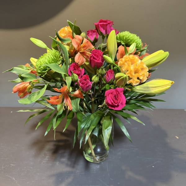Mixed bouquet of pink roses, orange alstroemeria, and yellow blooms in a glass vase