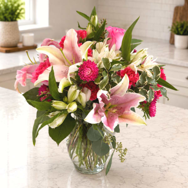 Pink lilies and mixed blooms arranged in a clear glass vase