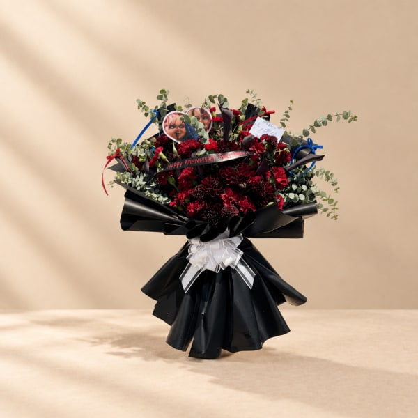 Red flower bouquet with black wrapping and a white ribbon