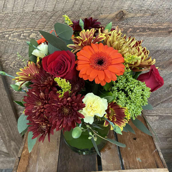 Mixed bouquet of red, orange, and yellow flowers in a green glass vase