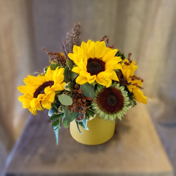 Yellow sunflowers arranged in a round yellow vase
