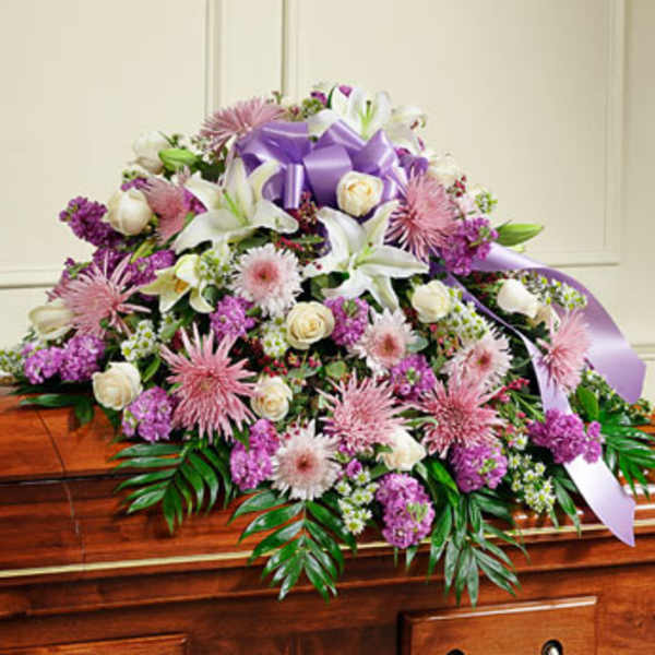 Large white and pink floral spray with a purple ribbon on a casket