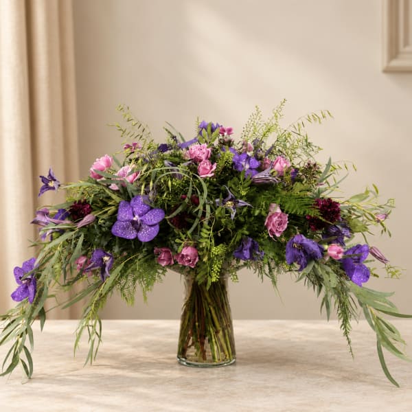 Large purple and pink floral arrangement in a clear glass vase