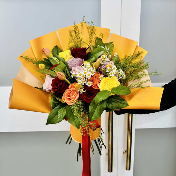 Hand-tied bouquet of mixed roses and small daisies wrapped in yellow paper