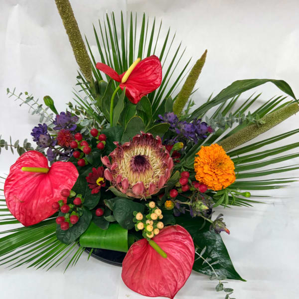 Tropical floral arrangement with red anthuriums, a protea, and orange marigold-like blooms