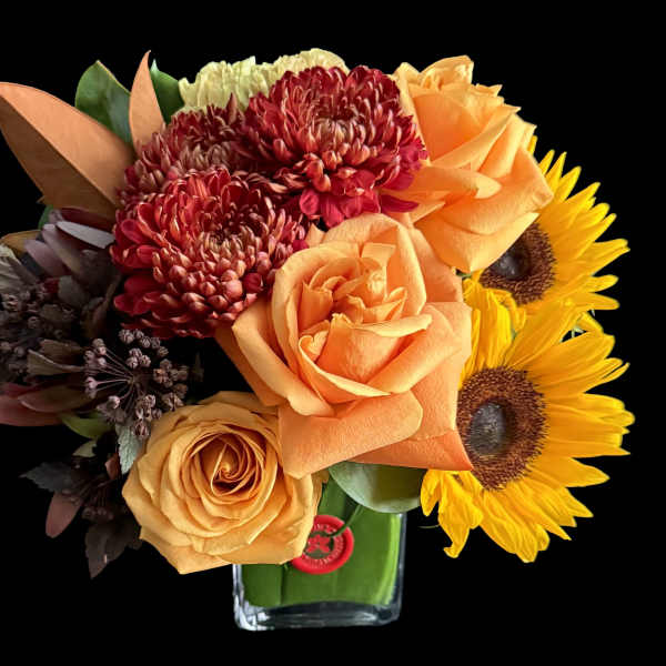 Orange roses, red chrysanthemums, and sunflowers in a glass vase