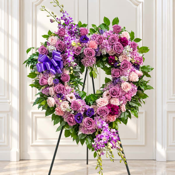 Heart-shaped floral wreath with purple and pink roses on a stand