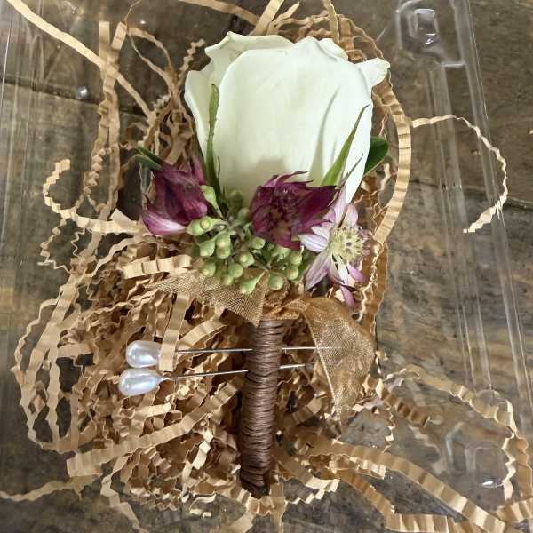 White rose boutonniere with purple flowers in a clear plastic box