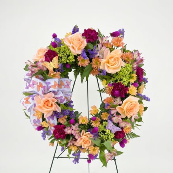 Butterfly-themed floral wreath with peach roses and purple flowers on an easel