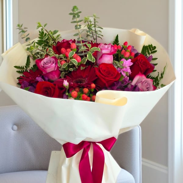 Bouquet of red and pink roses wrapped in white paper with a magenta ribbon