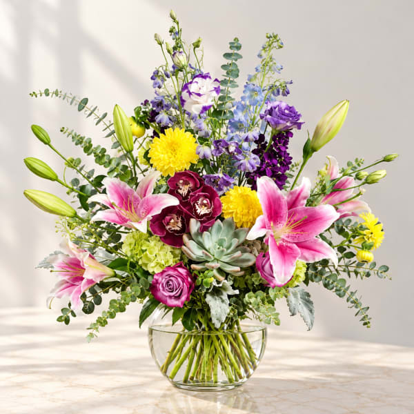 Mixed bouquet in a clear glass vase with lilies, roses, and purple blooms