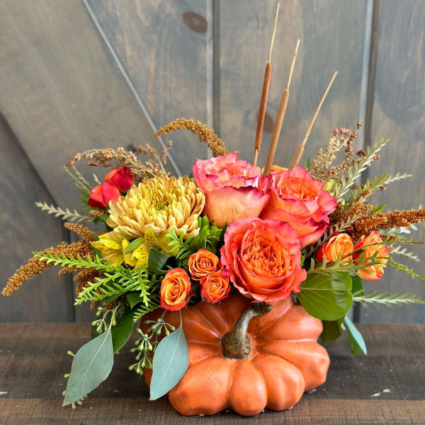 Orange pumpkin container with pink and orange flowers and dried accents