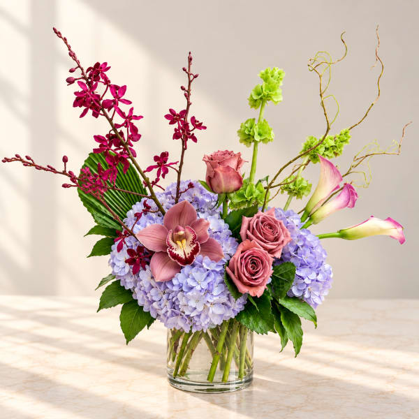 Mixed bouquet in a clear glass vase with pink orchids, roses, calla lilies, and lavender hydrangeas
