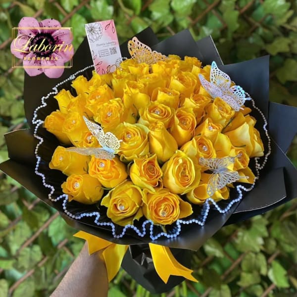 Bouquet of yellow roses wrapped in black paper with butterfly picks