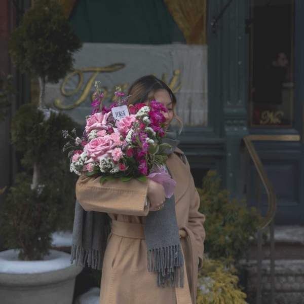 Woman holding a pink bouquet wrapped in tan paper outdoors