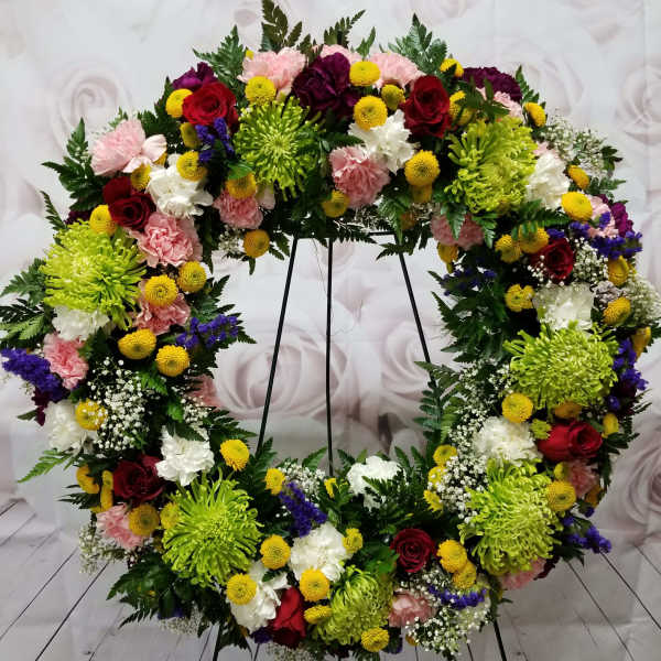 Large floral wreath on a stand with red, pink, white, and yellow blooms