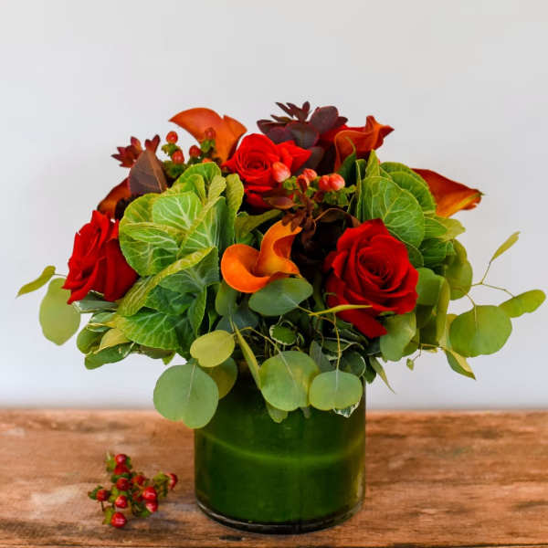 Red roses and orange calla lilies in a green glass vase