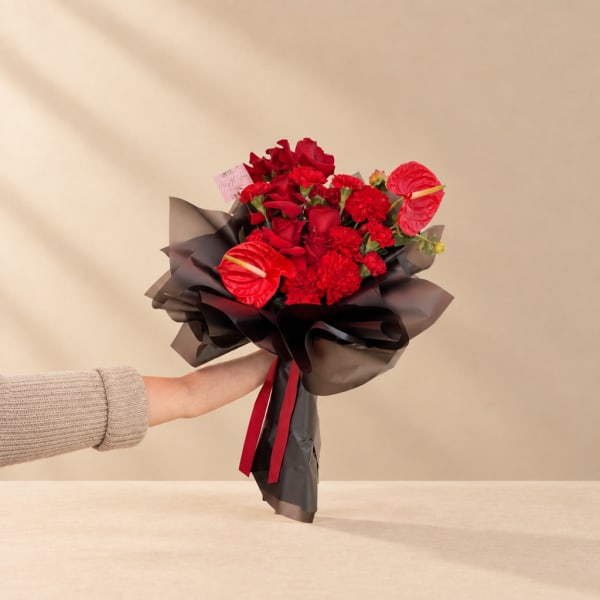Red flower bouquet wrapped in dark paper with a ribbon