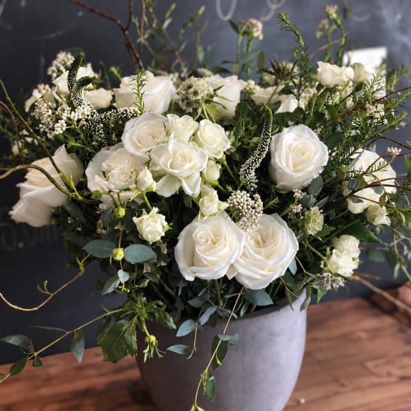 White roses and small white blooms arranged in a gray vase