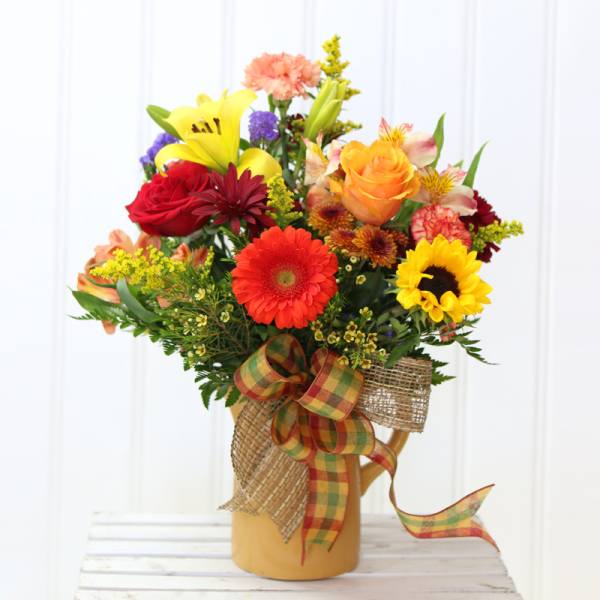 Colorful mixed bouquet in a tan pitcher with a plaid ribbon