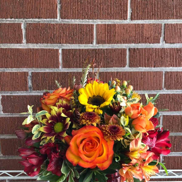 Mixed bouquet with orange roses and a sunflower in a burgundy vase