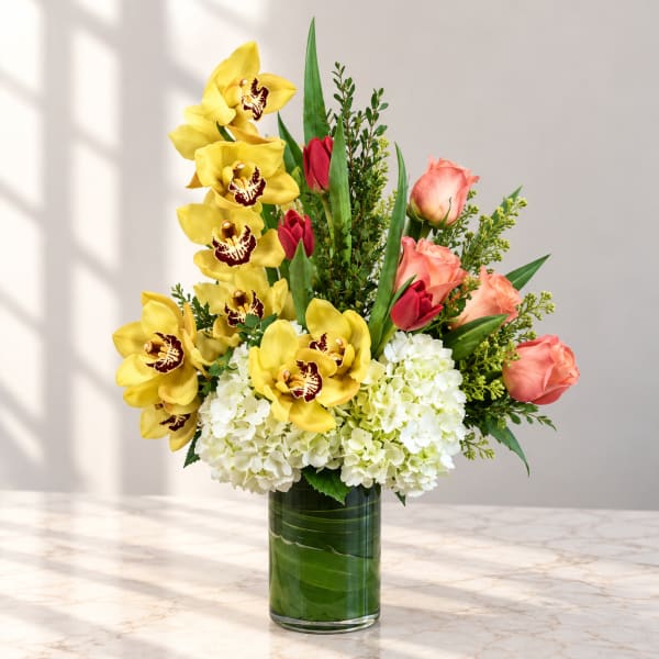 Yellow orchids and pink roses in a glass vase with white hydrangeas