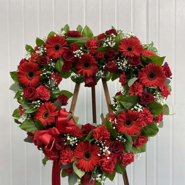 Heart-shaped red flower wreath on a wooden stand with ribbon