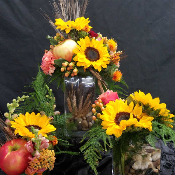 Sunflower arrangements in glass vases with apples and decorative grasses