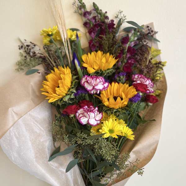 Bouquet of yellow sunflowers, pink carnations, and purple flowers wrapped in paper