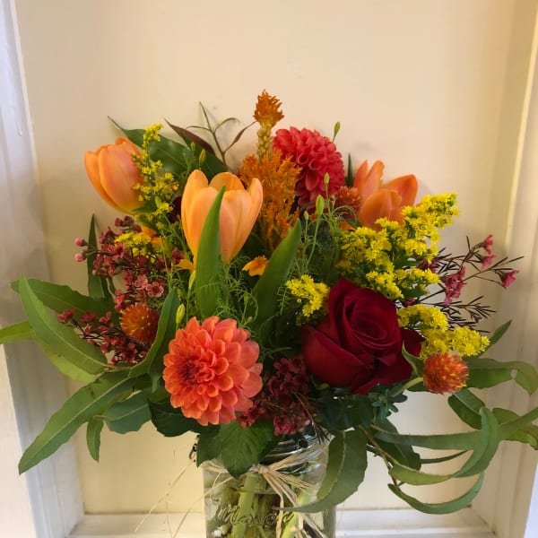 Mixed bouquet of orange tulips, red roses, and a peach dahlia in a glass jar
