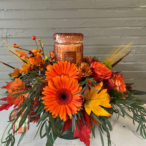 Orange floral arrangement with a pumpkin spice candle in a glass jar