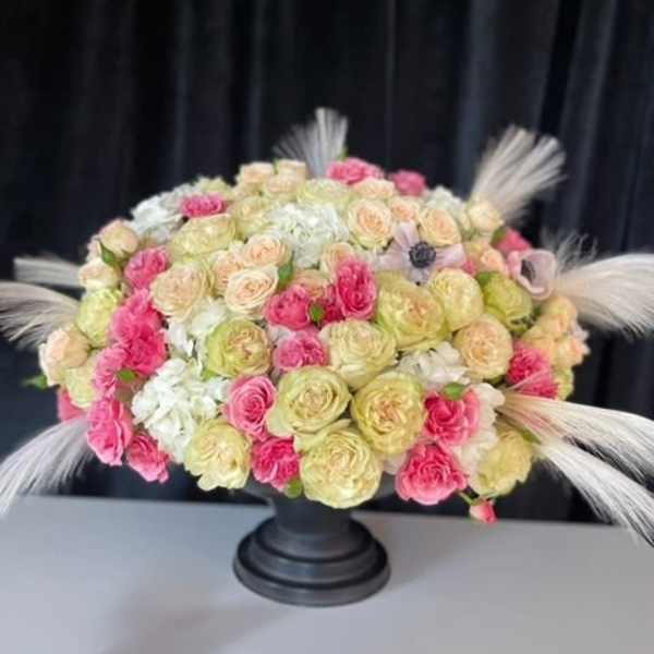 Round bouquet of pink, cream, and white roses in a black pedestal vase