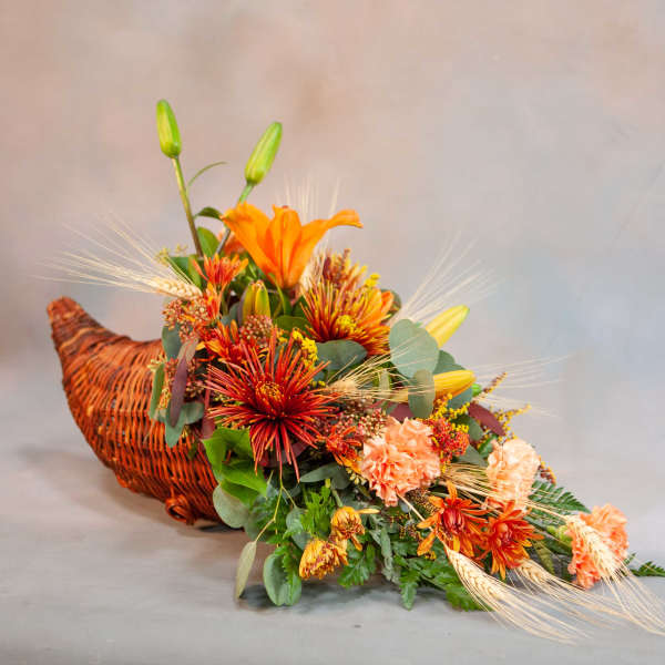 Orange floral arrangement in a woven basket with lilies and mums