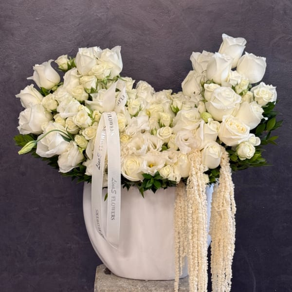 White rose arrangement in a white vase with trailing cream accents