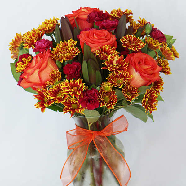 Bouquet of orange roses and red chrysanthemums in a glass vase with an orange ribbon