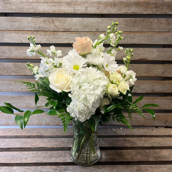 White floral arrangement in a clear glass vase with roses and daisies