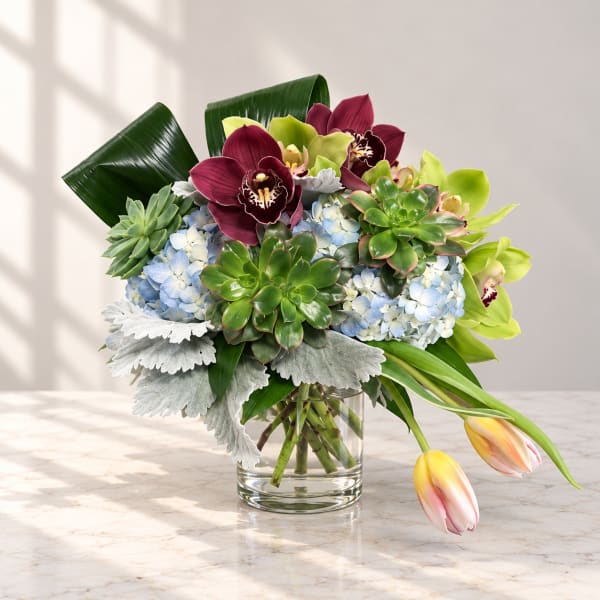 Bouquet of orchids, hydrangeas, succulents, and tulips in a glass vase