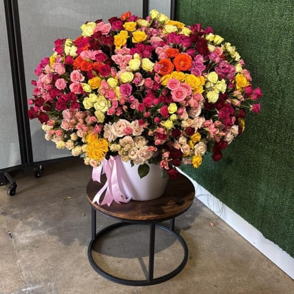 Large mixed rose arrangement in a white vase with a pink ribbon
