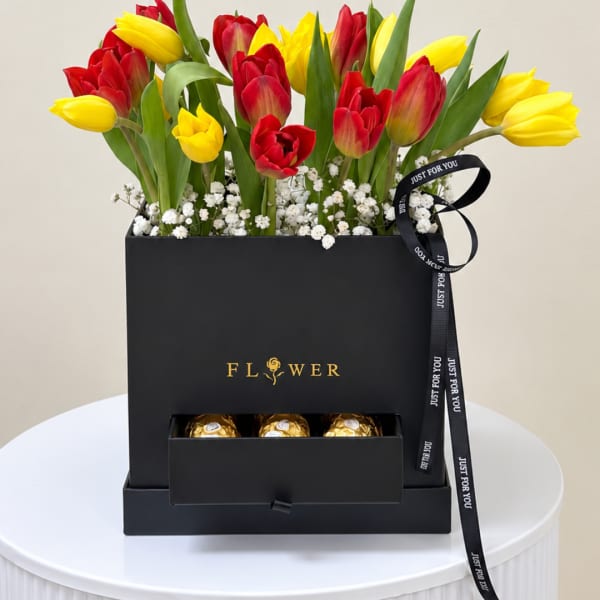 Red and yellow tulips in a black gift box with chocolates and ribbon