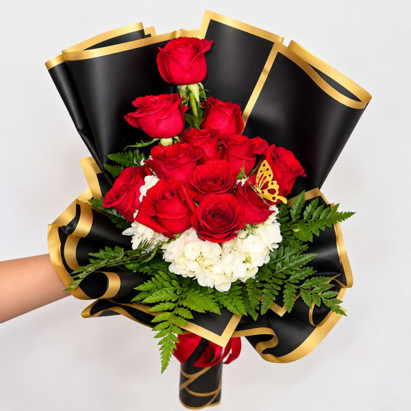 Bouquet of red roses and white hydrangeas wrapped in black paper with gold trim