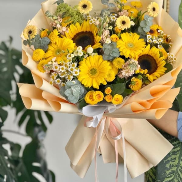Bouquet of yellow sunflowers and daisies wrapped in peach paper